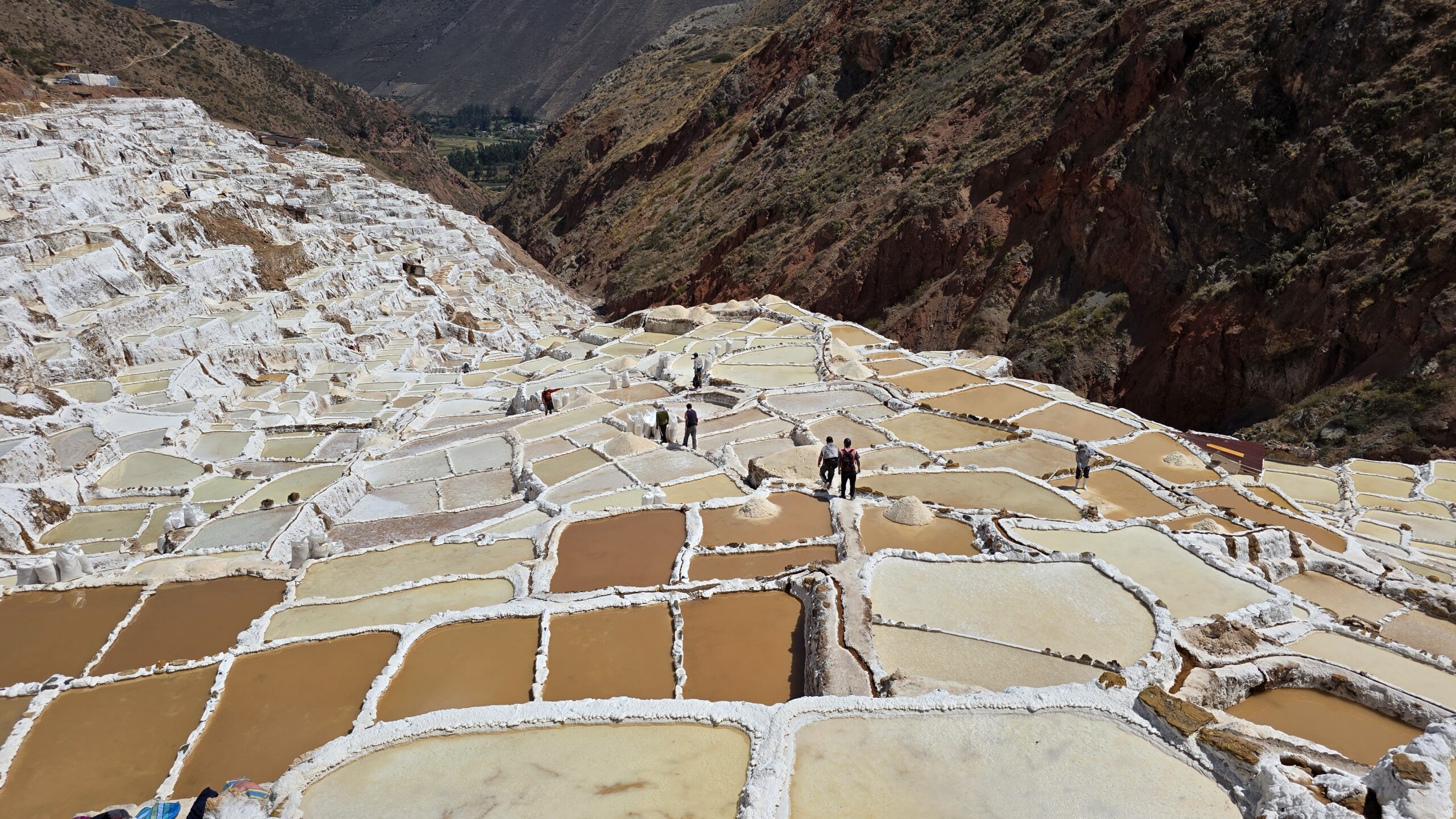 Las salineras de Maras descienden por la quebrada como un damero de pozas blancas, ocres y doradas. Unos viajeros caminan por los senderos de sal.