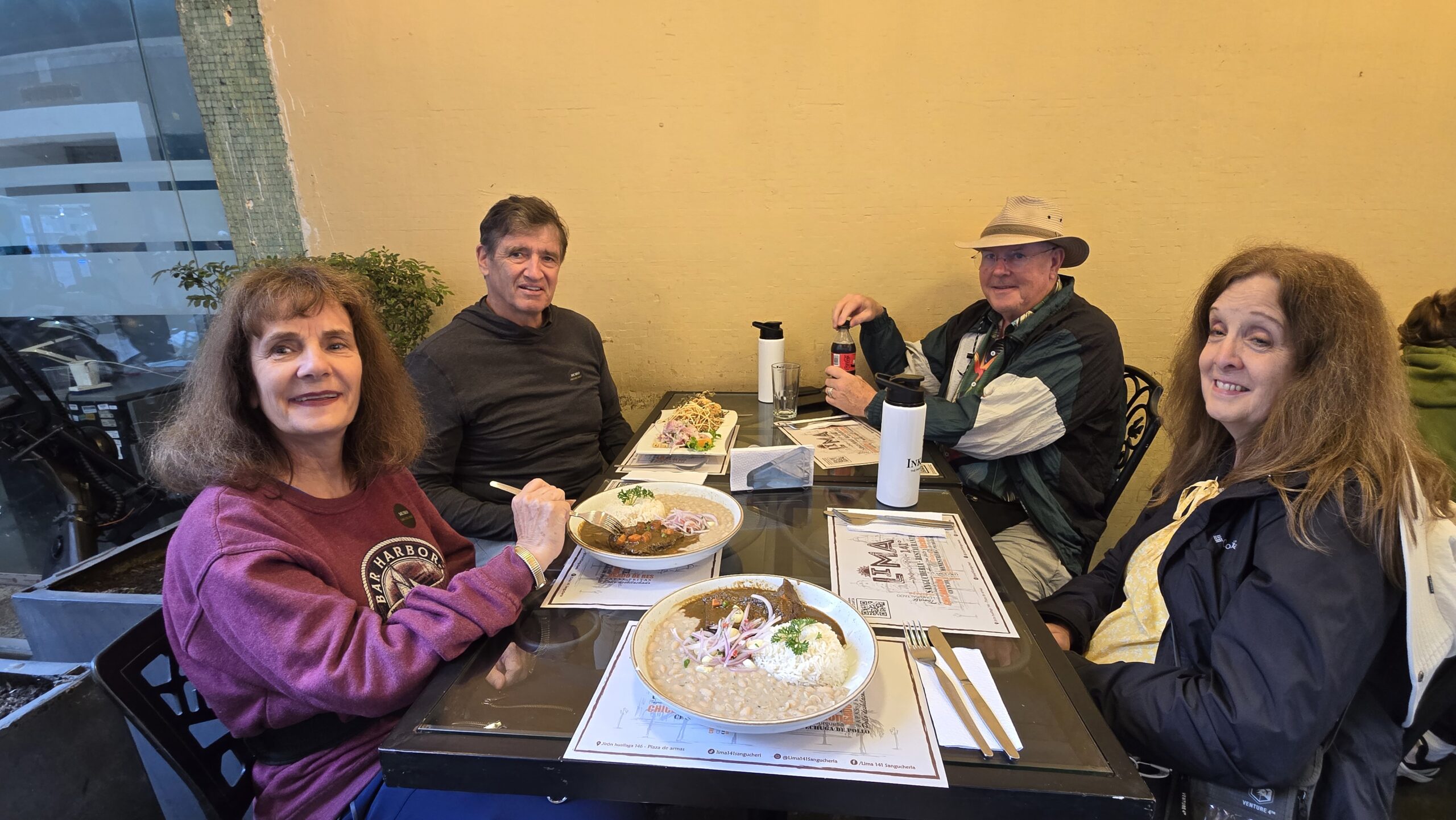 Cuatro viajeros almuerzan en un restaurante de Lima, con platos peruanos sobre la mesa. El local tiene las paredes amarillas.