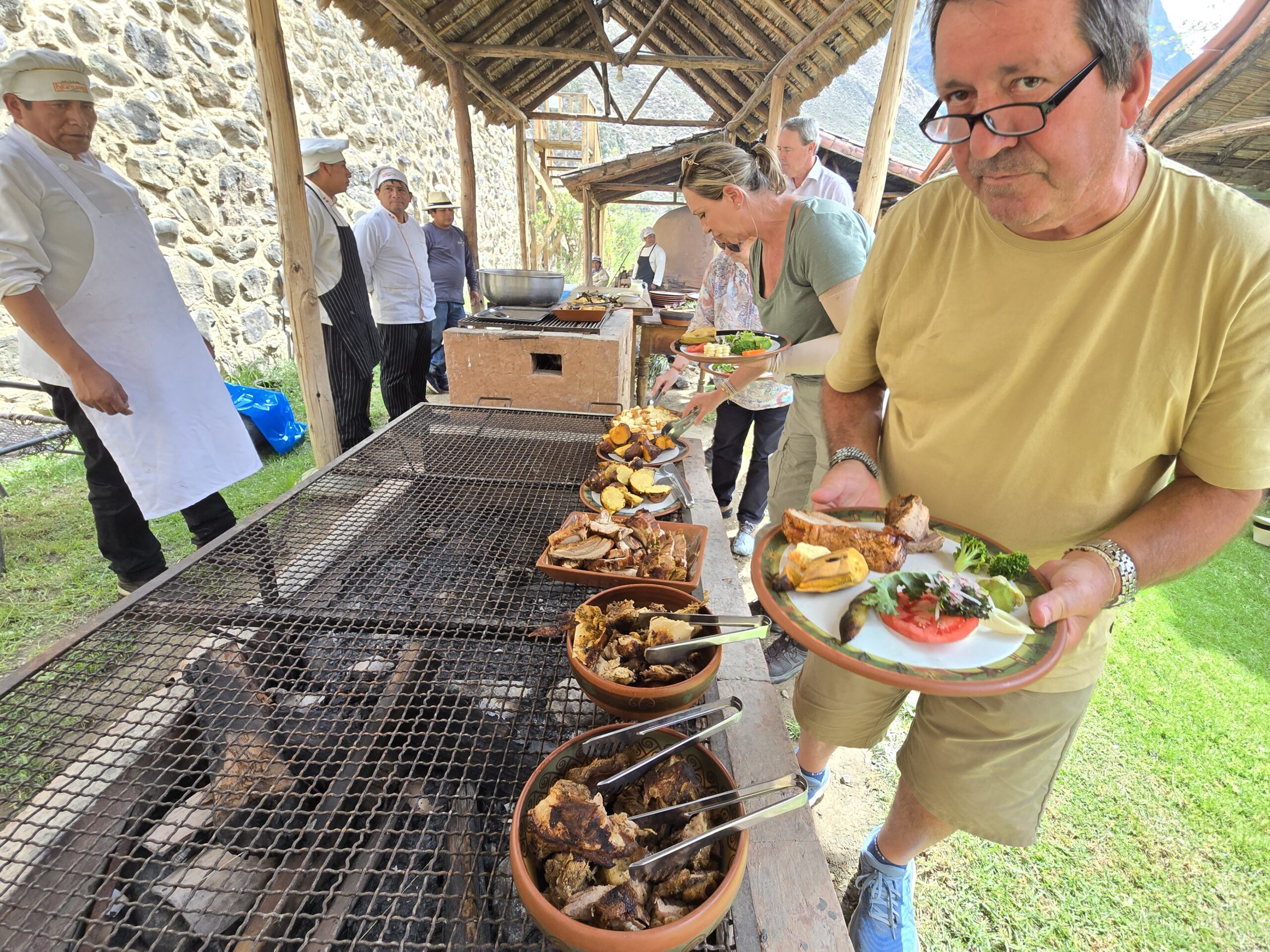 Una mesa con mantel blanco está lista bajo una sombrilla, en un jardín del Valle Sagrado. Detrás se ven los árboles y los cerros.