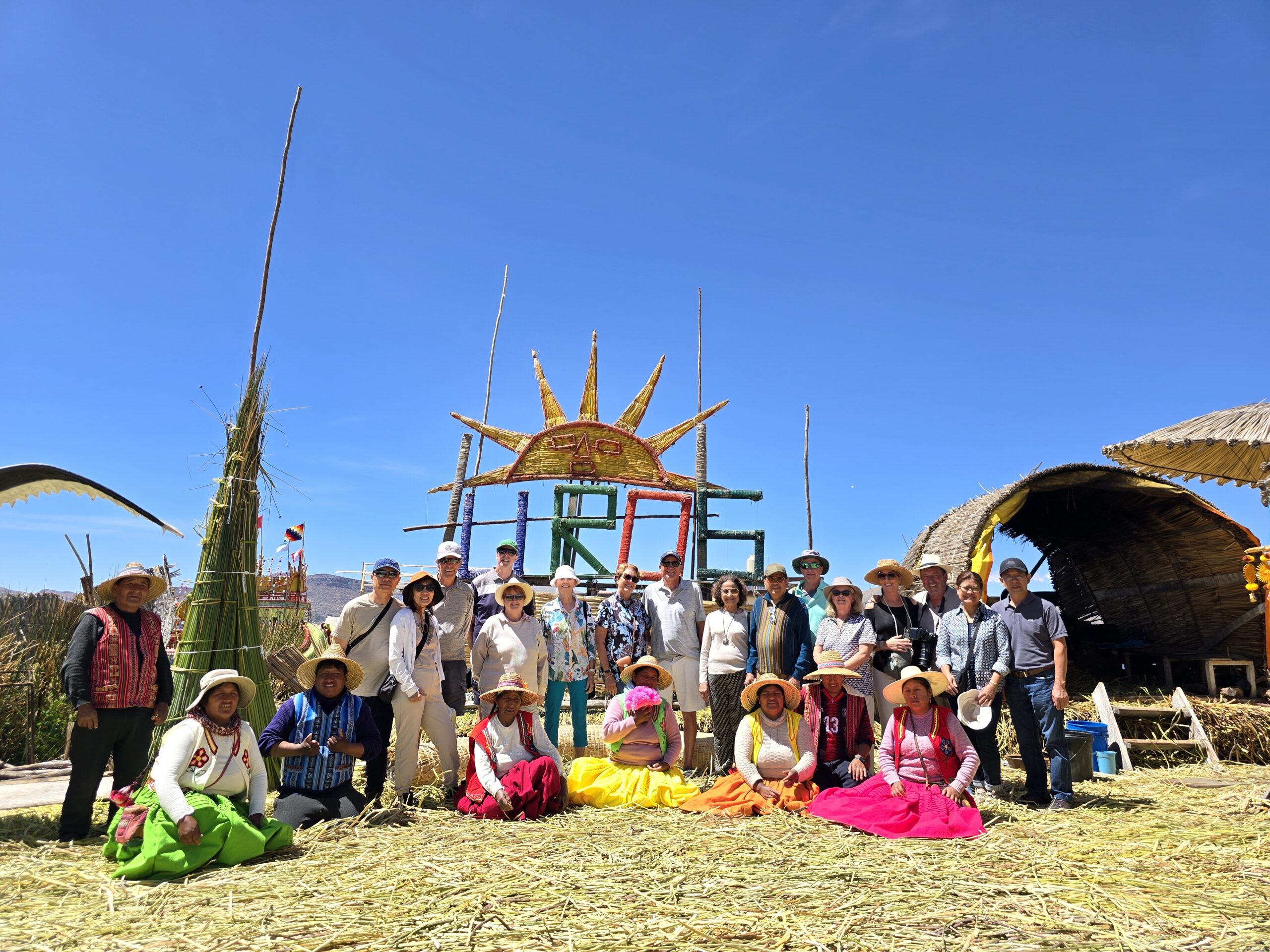 En las islas de los Uros, el grupo se reúne ante un sol tejido en totora. Adelante, mujeres de polleras de colores; detrás, los viajeros, bajo un cielo muy azul.