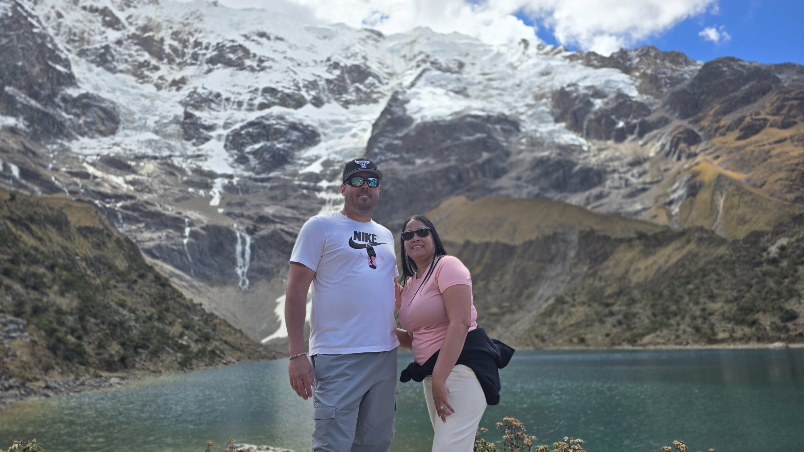 Una pareja posa frente a la laguna Humantay, de agua turquesa. Detrás se alza el nevado, con hielo y nieve.