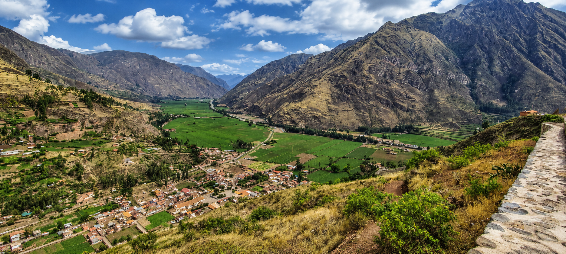 Desde un camino de piedra se ve el Valle Sagrado: un pueblo de tejas, chacras de un verde intenso y la cordillera cerrando el valle.