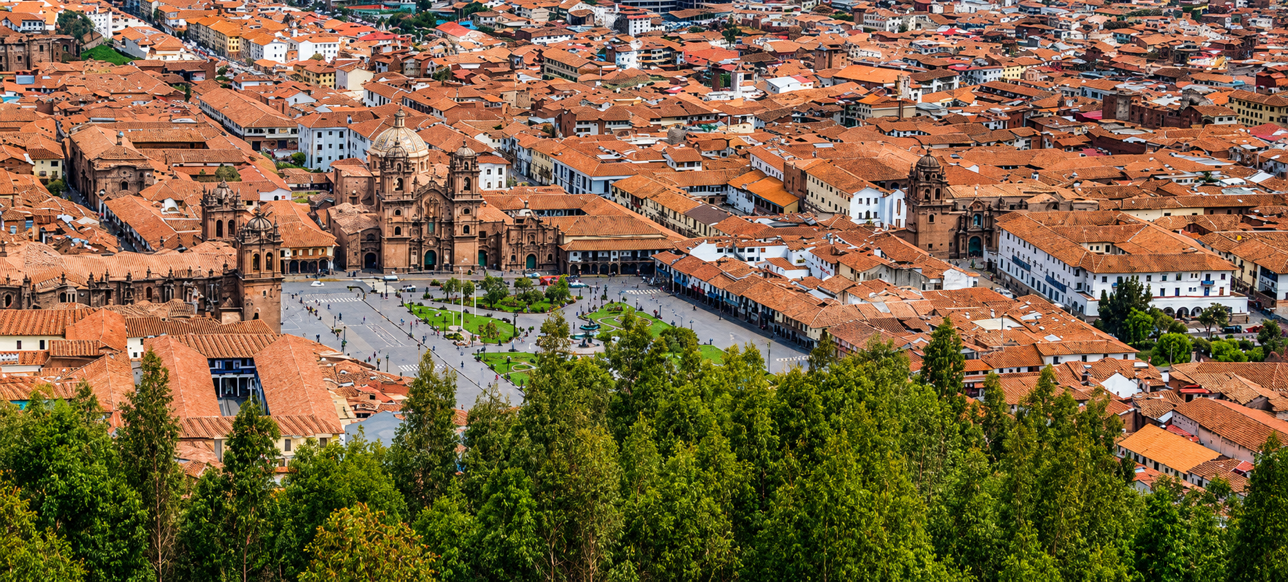 Cusco desde lo alto: un mar de tejas naranjas, la Catedral en el centro de la Plaza de Armas y el verde de los árboles en primer plano.