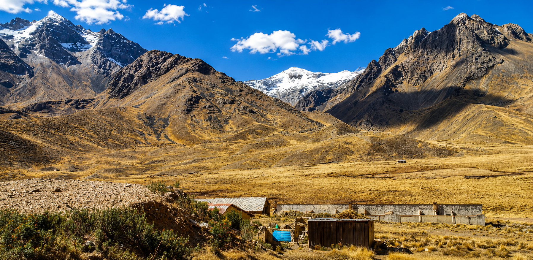 Una puna dorada se abre entre nevados, con casas rústicas al pie de la cordillera. El cielo está limpio sobre la ruta alta hacia Puno.