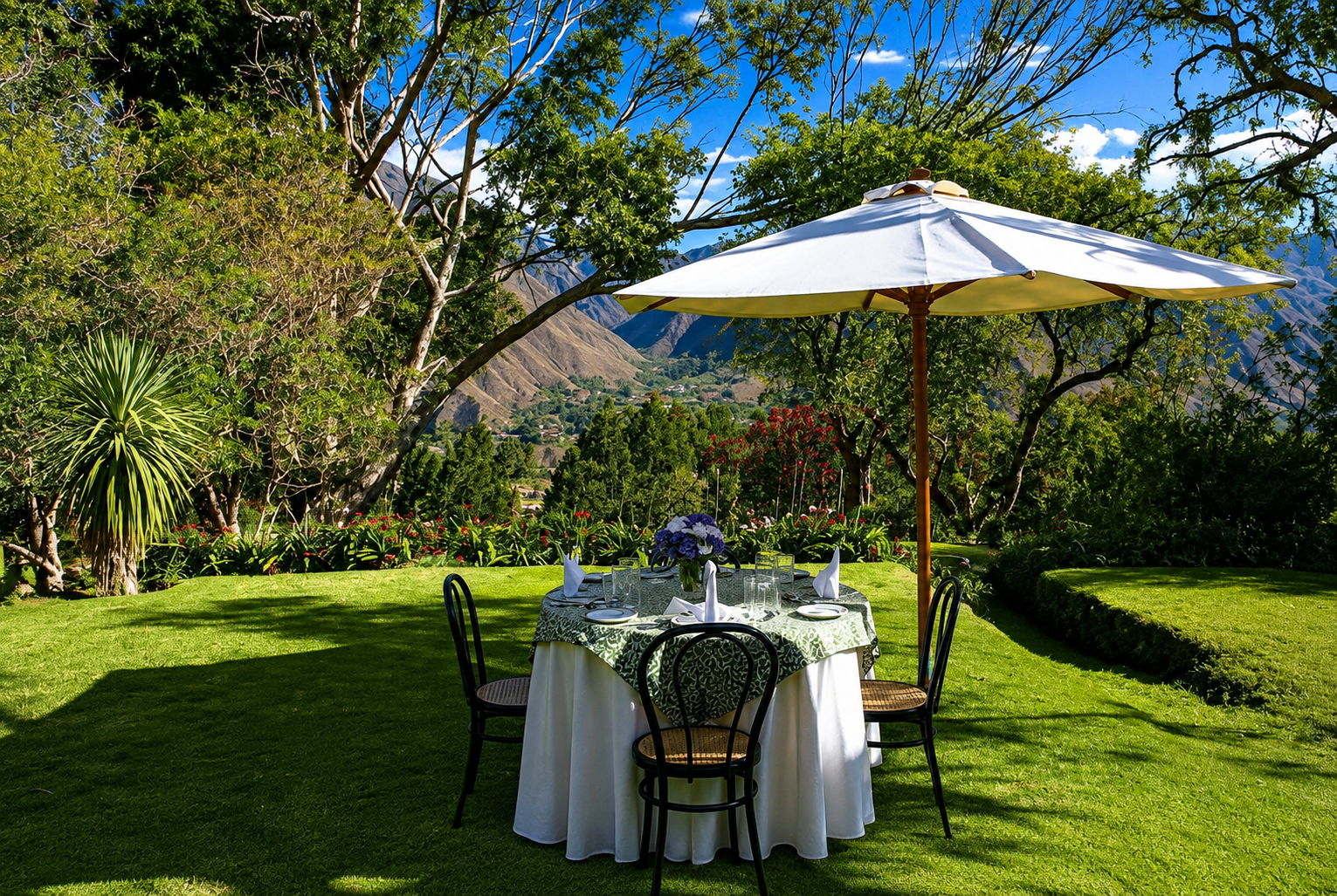 Una mesa con mantel blanco está lista bajo una sombrilla, en un jardín del Valle Sagrado. Detrás se ven los árboles y los cerros.