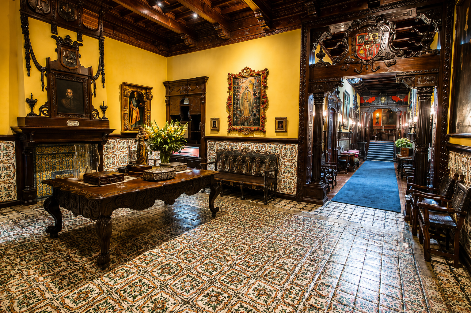 Un salón de la Casa Aliaga, con paredes amarillas, piso de azulejos y muebles de madera tallada. Al fondo, un pasillo con alfombra azul lleva hacia la escalera.