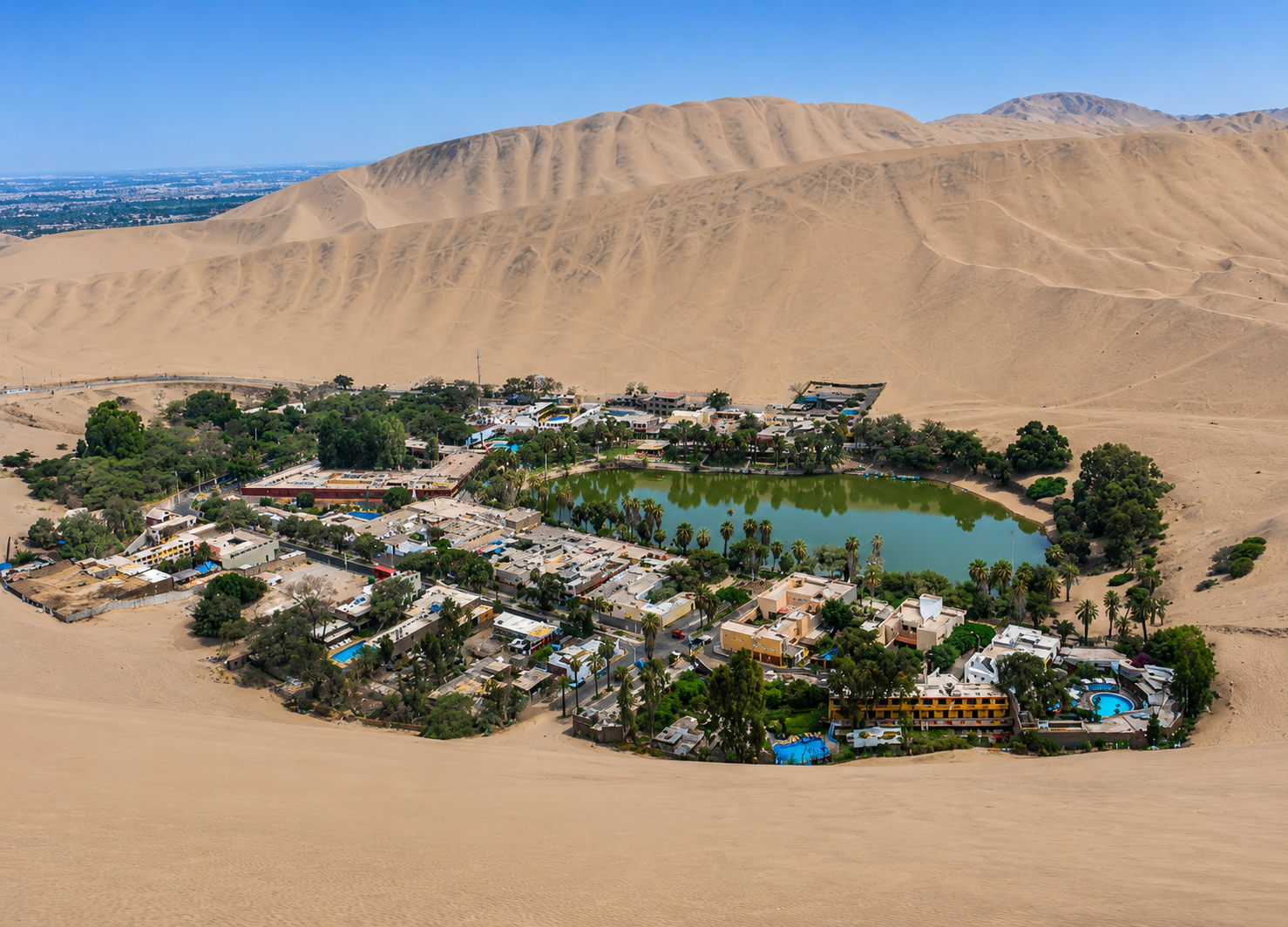 Huacachina se ve desde el aire: una laguna verde abrazada por palmeras y hoteles, en el hueco de las dunas de Ica.