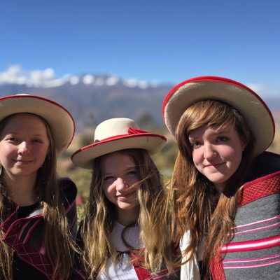 Tres viajeras posan con sombreros de ala ancha y ponchos rayados. Detrás, la cordillera nevada se ve bajo un cielo limpio.